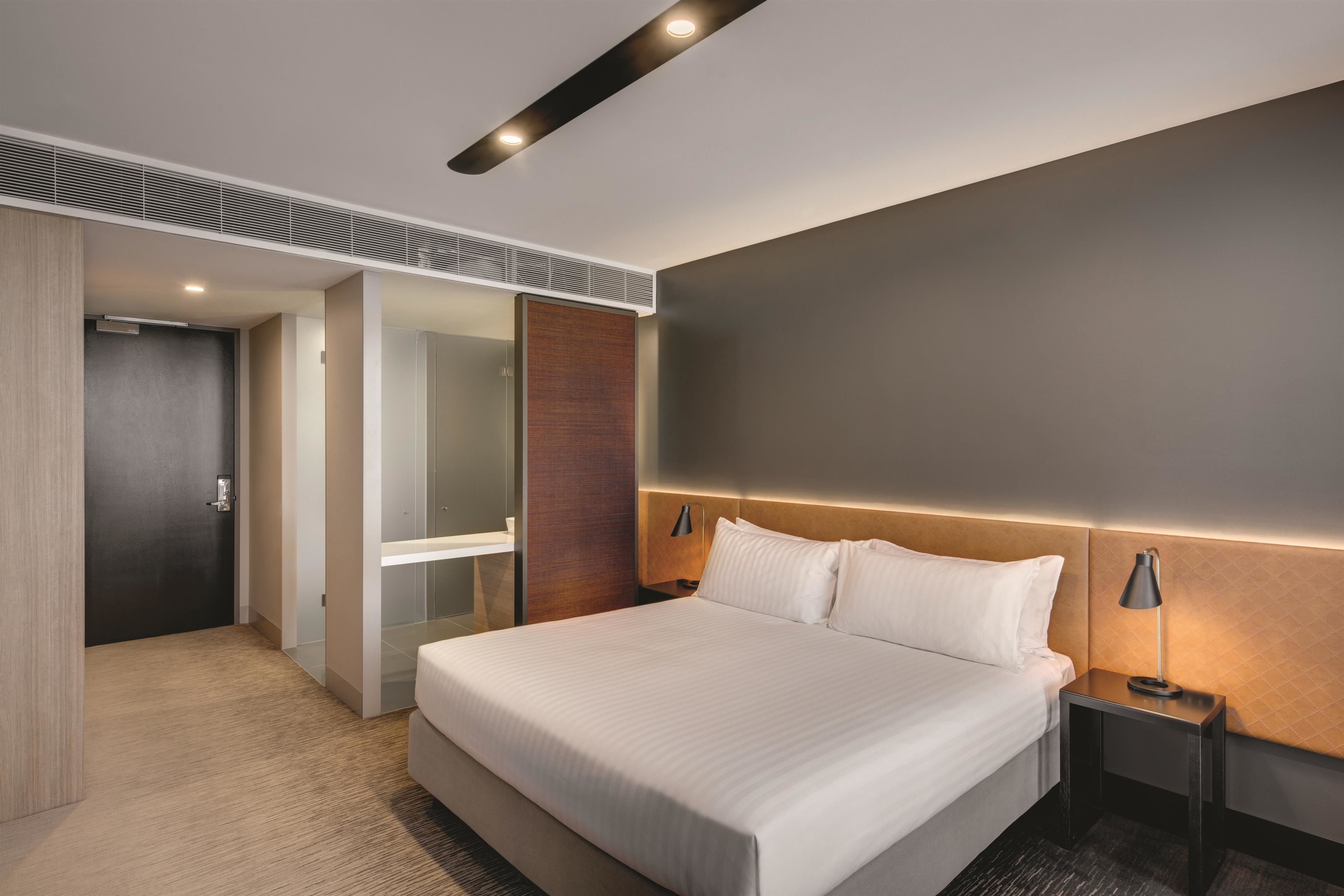 Ein modernes Hotelzimmer mit einem großen Bett, einem Nachttisch mit Lampe, einem Holz-Kopfteil und einem begehbaren Kleiderschrank.