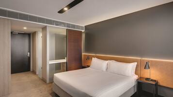Ein modernes Hotelzimmer mit einem großen Bett, einem Nachttisch mit Lampe, einem Holz-Kopfteil und einem begehbaren Kleiderschrank.