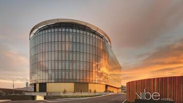 Experience the sleek, curved design of Vibe Hotel, set amidst lush greenery and a well-maintained road.