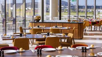 A restaurant with multiple tables set for dining, featuring a bar area with a large mirror and a view of the cityscape through large windows.