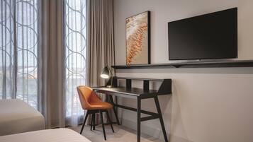 A hotel room with a bed, a desk with a chair, a TV, and a window with curtains.