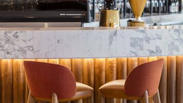 A bar area with a marble countertop, two red upholstered bar stools, and a variety of bottles and glasses in the background.