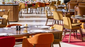 A modern dining area with large windows, multiple tables, and chairs.