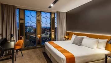 Habitació d'hotel amb un llit gran, una taula de treball i vista a través d'una porta de vidre.