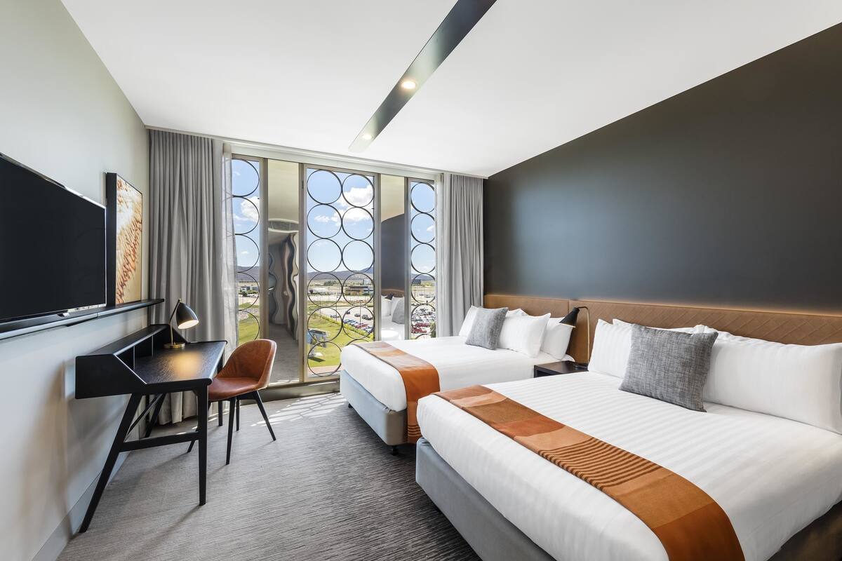 A hotel room with two beds, a desk, a chair, and a TV.