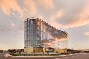A modern glass building with a curved facade, located at a road intersection. - Vibe Hotel Canberra (Canberra Airport)