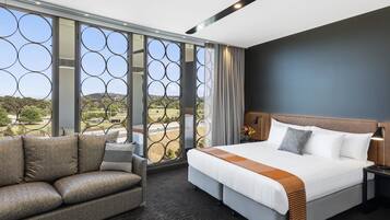 Ein Hotelzimmer mit einem großen Bett, einer Couch und Blick auf die Landschaft durch ein fenster mit Muster.