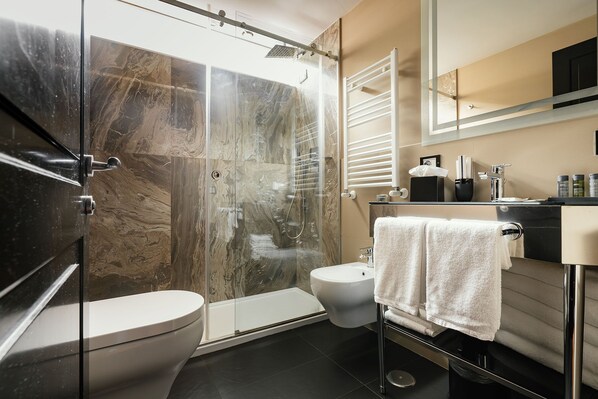 A modern bathroom with a glass-enclosed shower, a toilet, and a sink with a towel rack.
