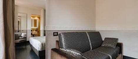 A hotel room with a sofa, a bed, a chair, and a mirror.