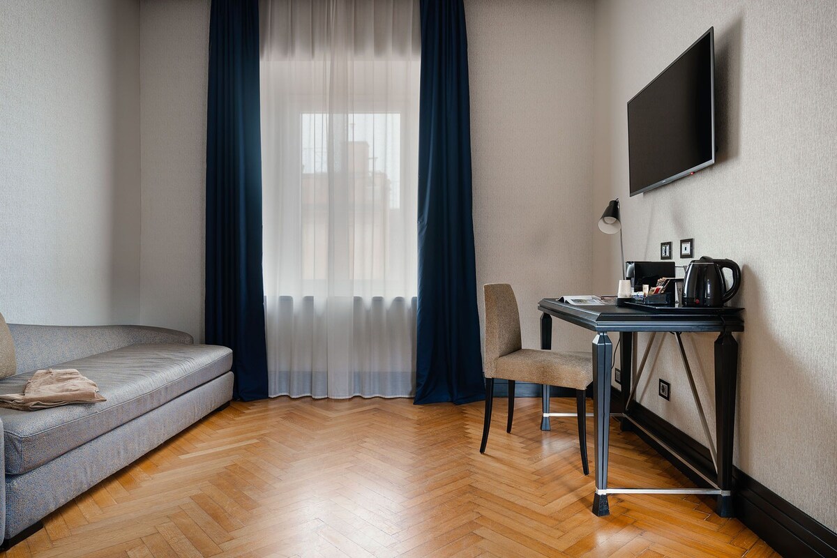A hotel room with a sofa, a desk with a coffee maker, and a TV on the wall.