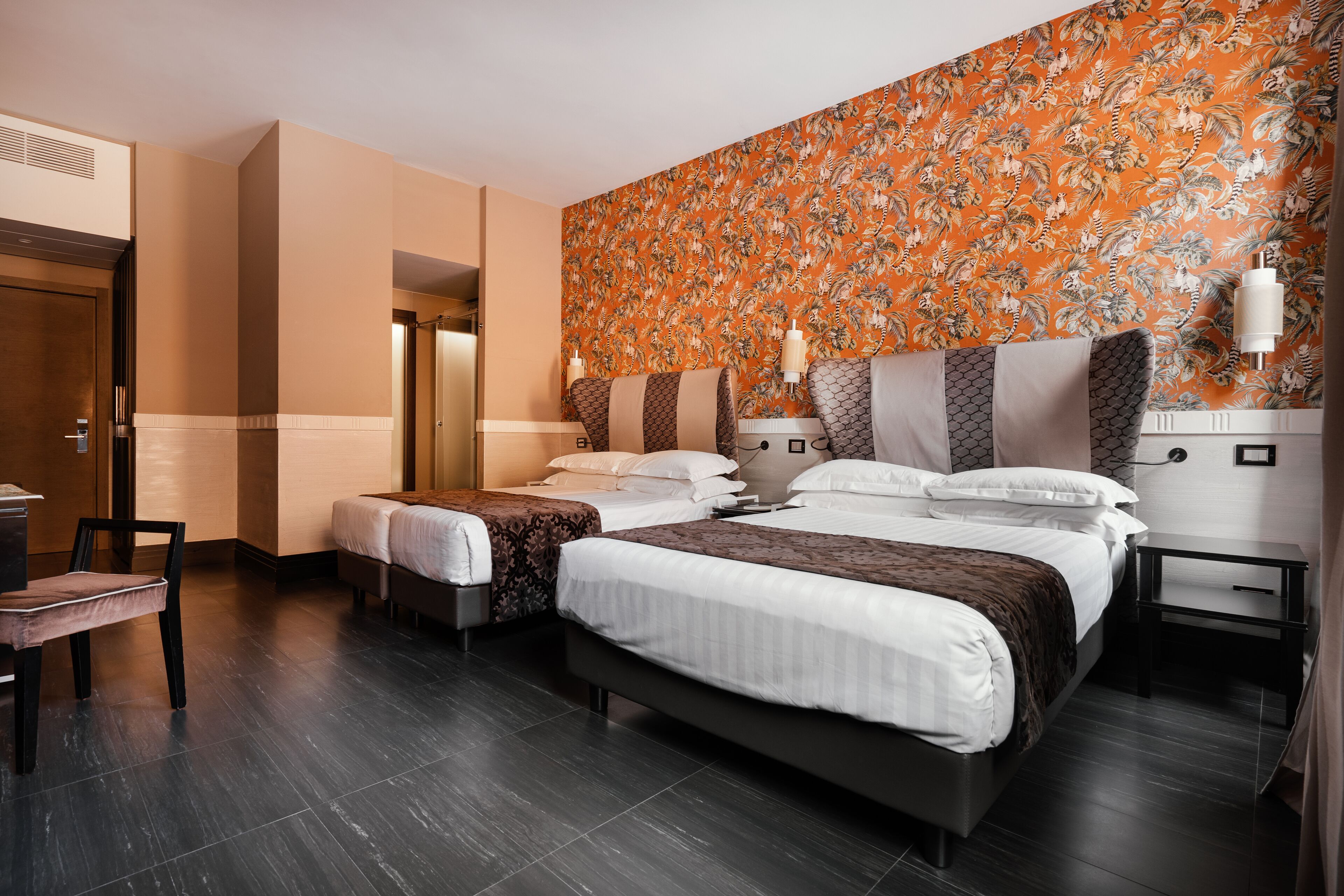 A hotel room with two beds, a desk, and a chair.