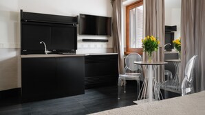 A modern kitchen with a black countertop, a built-in TV, and a dining area with clear chairs and a small table. - Unica Suites Rome (Rome)
