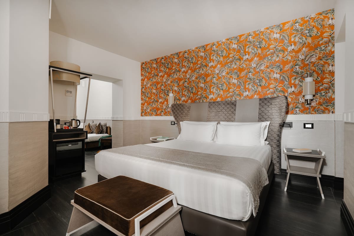 A hotel room with a large bed, a small desk, a mirror, and a decorative wall panel.