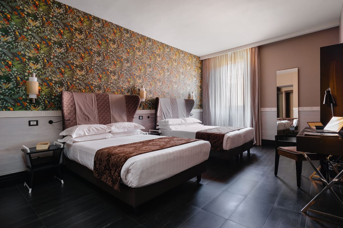 A hotel room with two beds, a desk, a chair, a lamp, and a mirror.