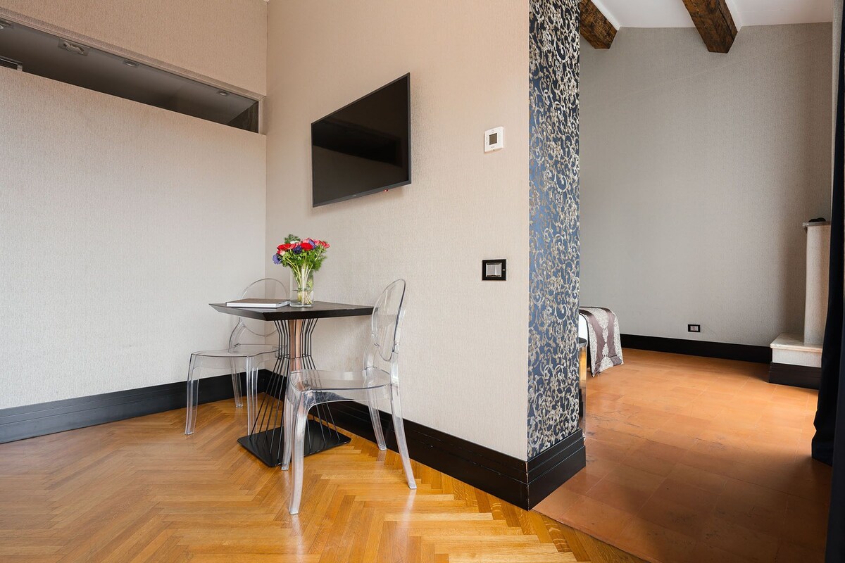 A modern room with a round table, clear chairs, a vase of flowers, and a flat-screen TV mounted on the wall.