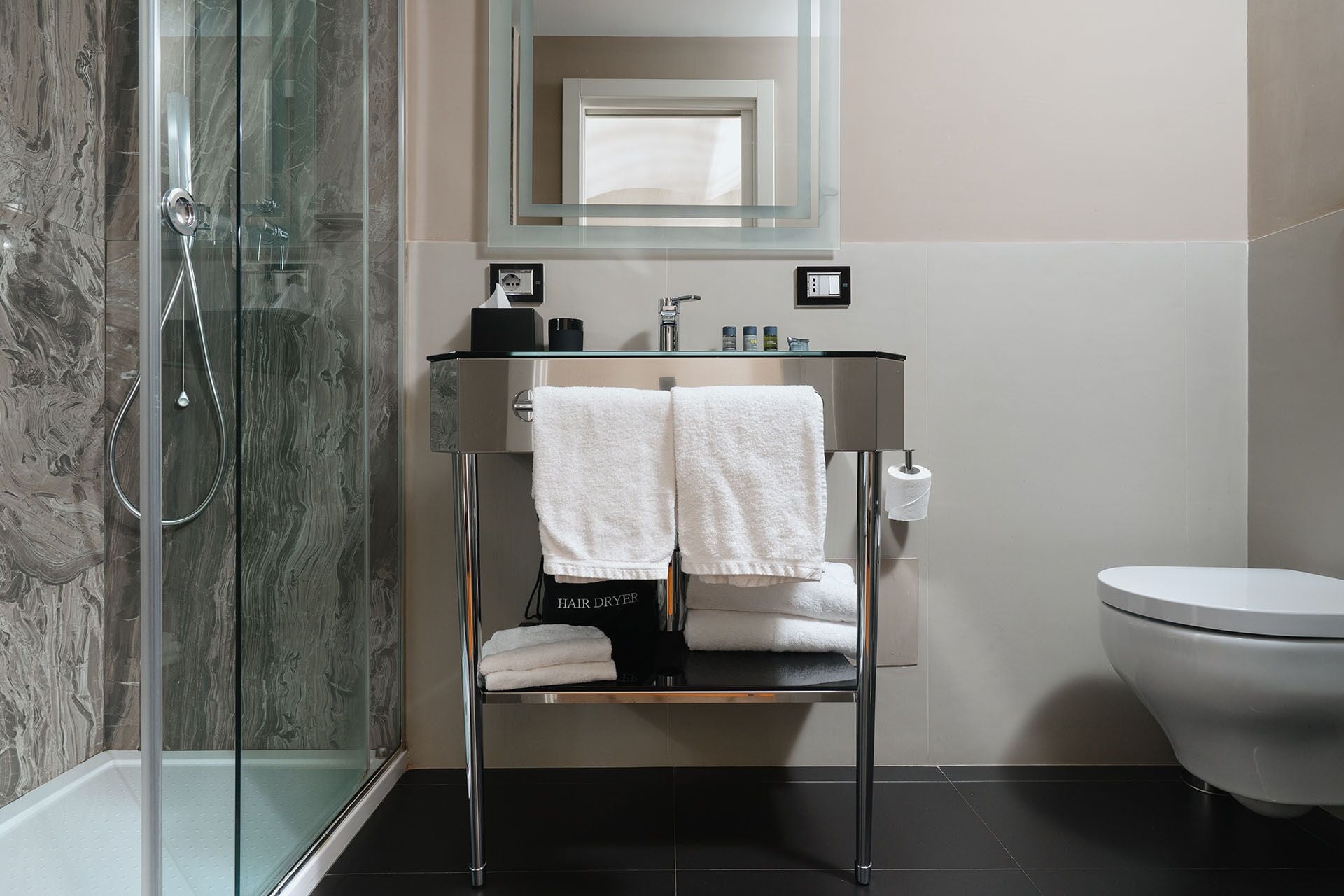 A modern bathroom with a glass shower enclosure, a glass-topped sink with two white towels, a mirror, and a toilet.