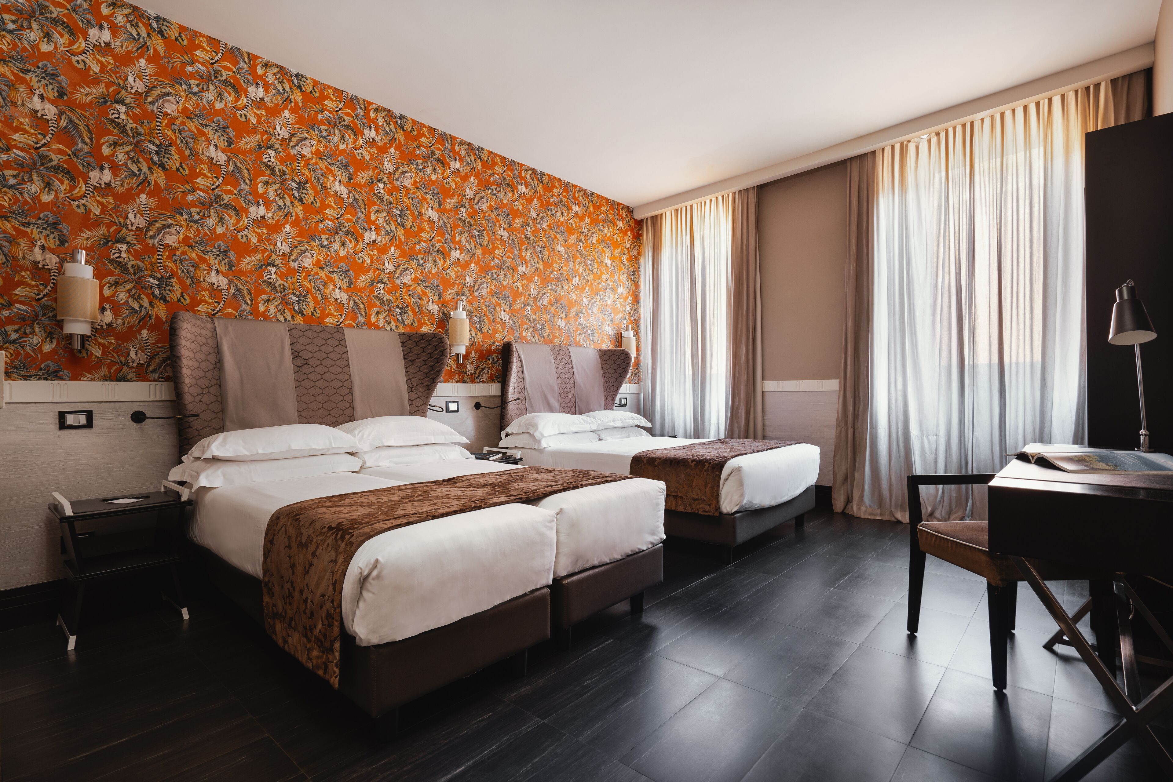 Een hotelkamer met twee bedden, een bureau en een groot raam met gordijnen.
