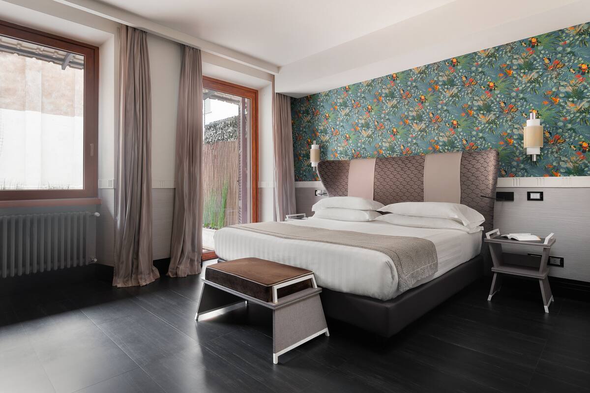 A modern bedroom with a large bed, a bedside table, a nightstand, and a window with curtains.