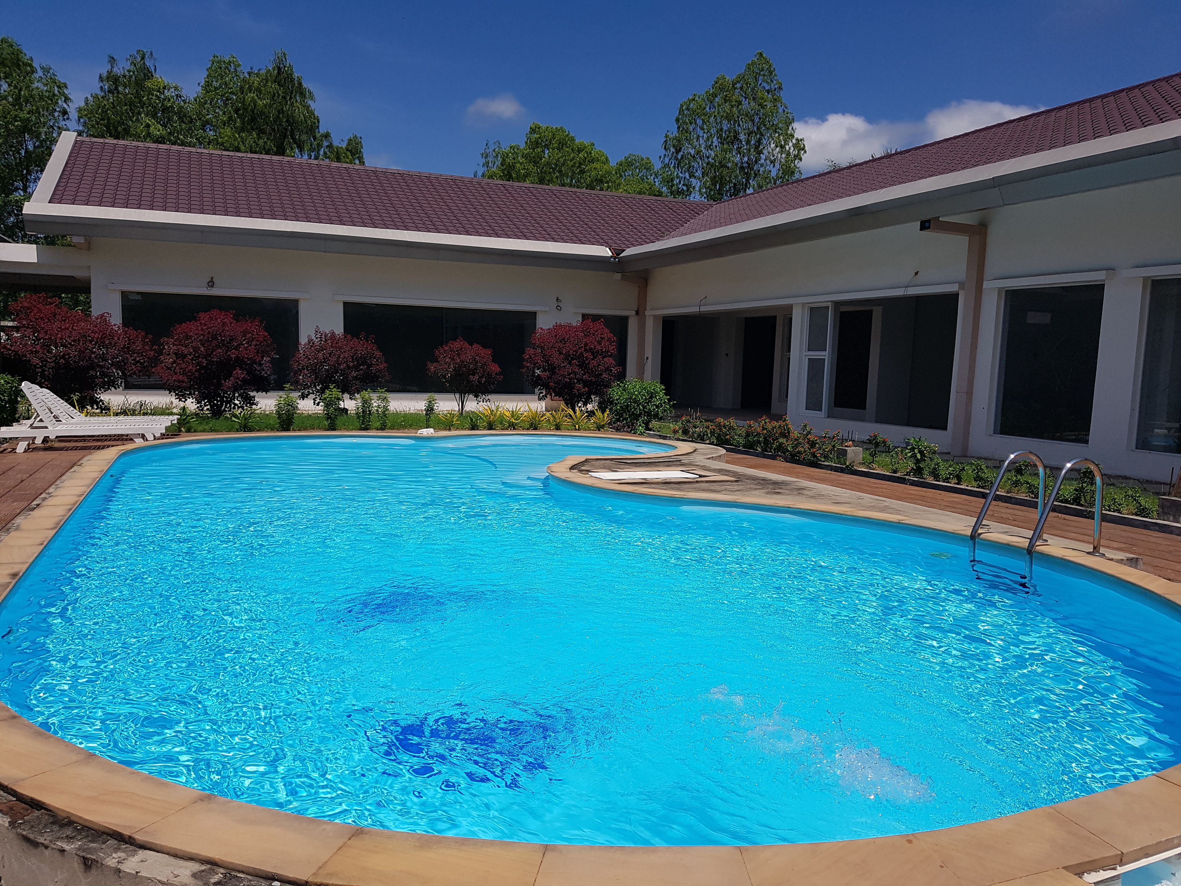 Una piscina con borde de baldosas, rodeada por un porche cubierto con amplias ventanas y techo de tejas rojas.