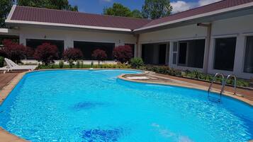 Una piscina con borde de baldosas, rodeada por un porche cubierto con amplias ventanas y techo de tejas rojas.
