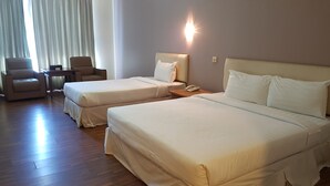 Une chambre d’hôtel avec deux lits, un bureau, une chaise et une lampe.
