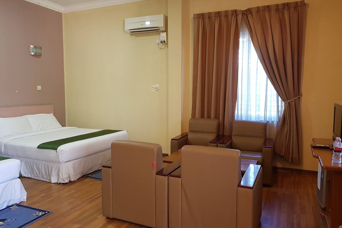 Une chambre d’hôtel avec un lit, deux fauteuils, une petite table et un téléviseur.