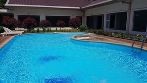 Une piscine à l’eau d’un bleu cristallin, entourée d’un bâtiment doté de grandes fenêtres et d’un patio couvert.