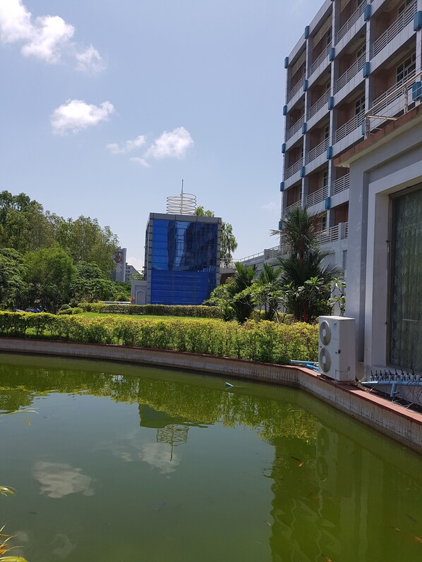 A modern building with a blue glass facade, surrounded by greenery and a water feature.