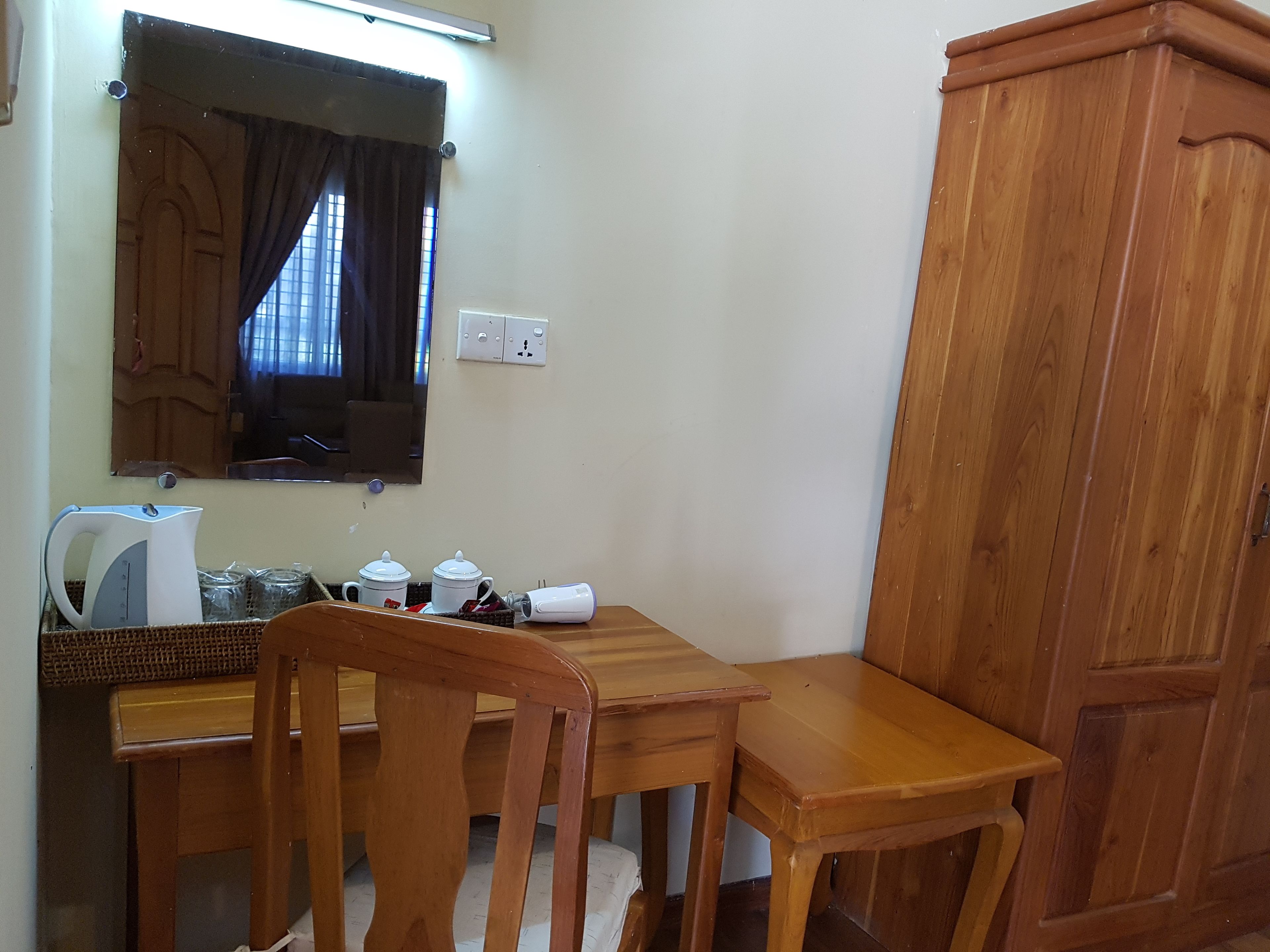 Una habitación pequeña y ordenada con una mesa de madera, dos sillas, un hervidor y un armario.