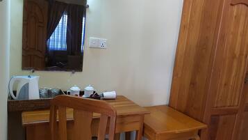 Una habitación pequeña y ordenada con una mesa de madera, dos sillas, un hervidor y un armario.