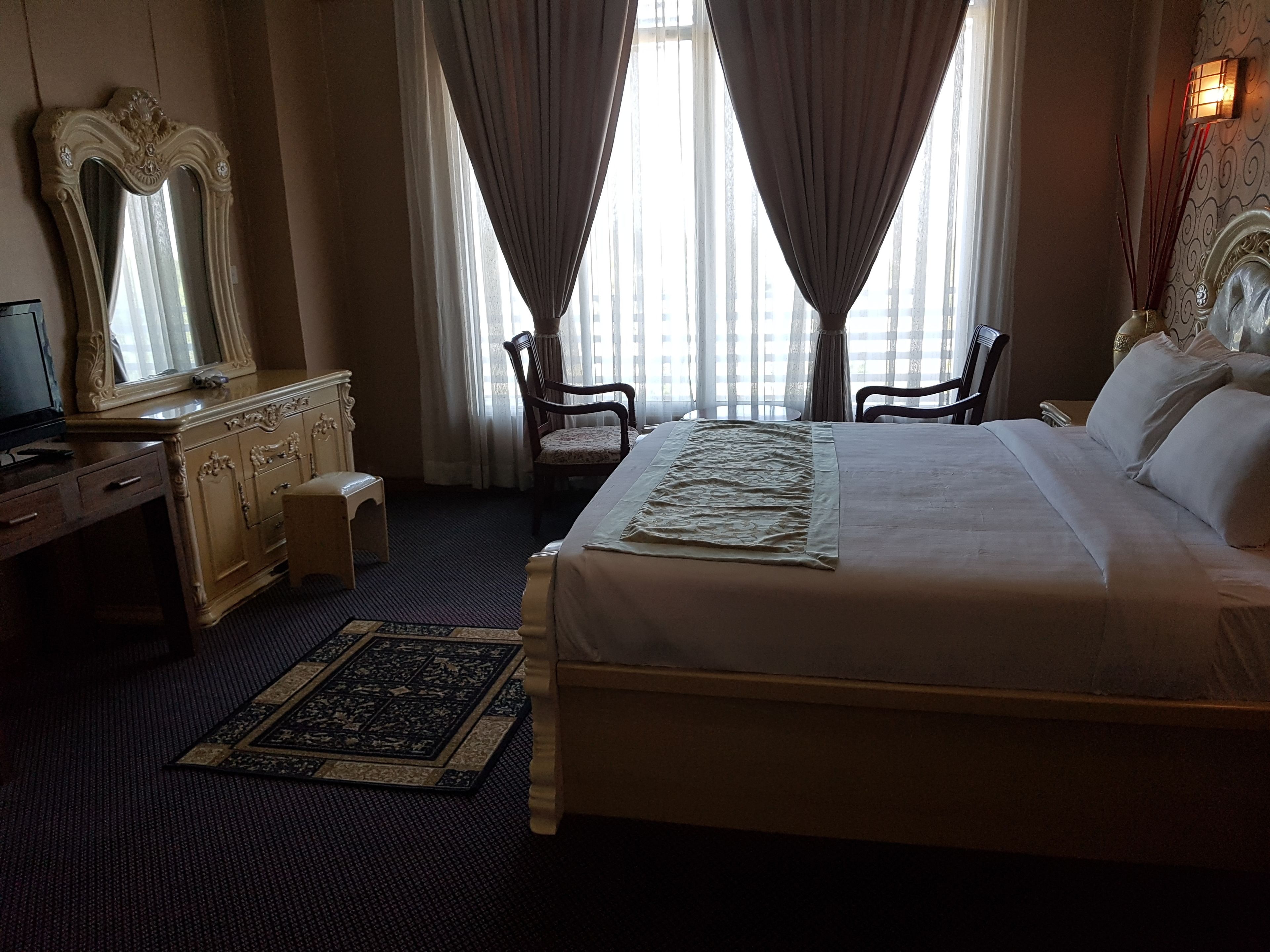A hotel room with a large bed, a dresser with a mirror, a chair, and a desk.