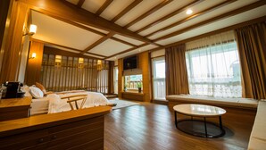 Une chambre d’hôtel avec un plafond en bois, un lit avec du linge de maison blanc, une petite table, un canapé et un téléviseur fixé au mur.