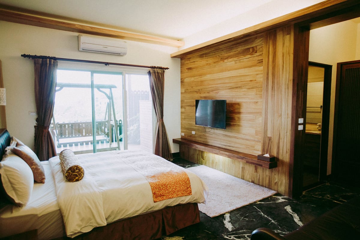 Une chambre d’hôtel avec un lit, un téléviseur fixé au mur en bois et un balcon avec des rideaux.