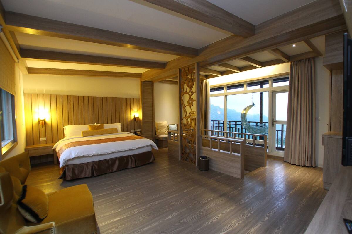 Une chambre d’hôtel avec un grand lit, un coin salon, un balcon avec vue et des boiseries.