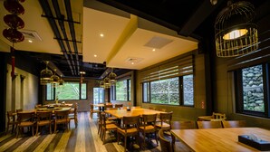 Un restaurant avec des tables et des chaises en bois, de grandes fenêtres et des luminaires suspendus.