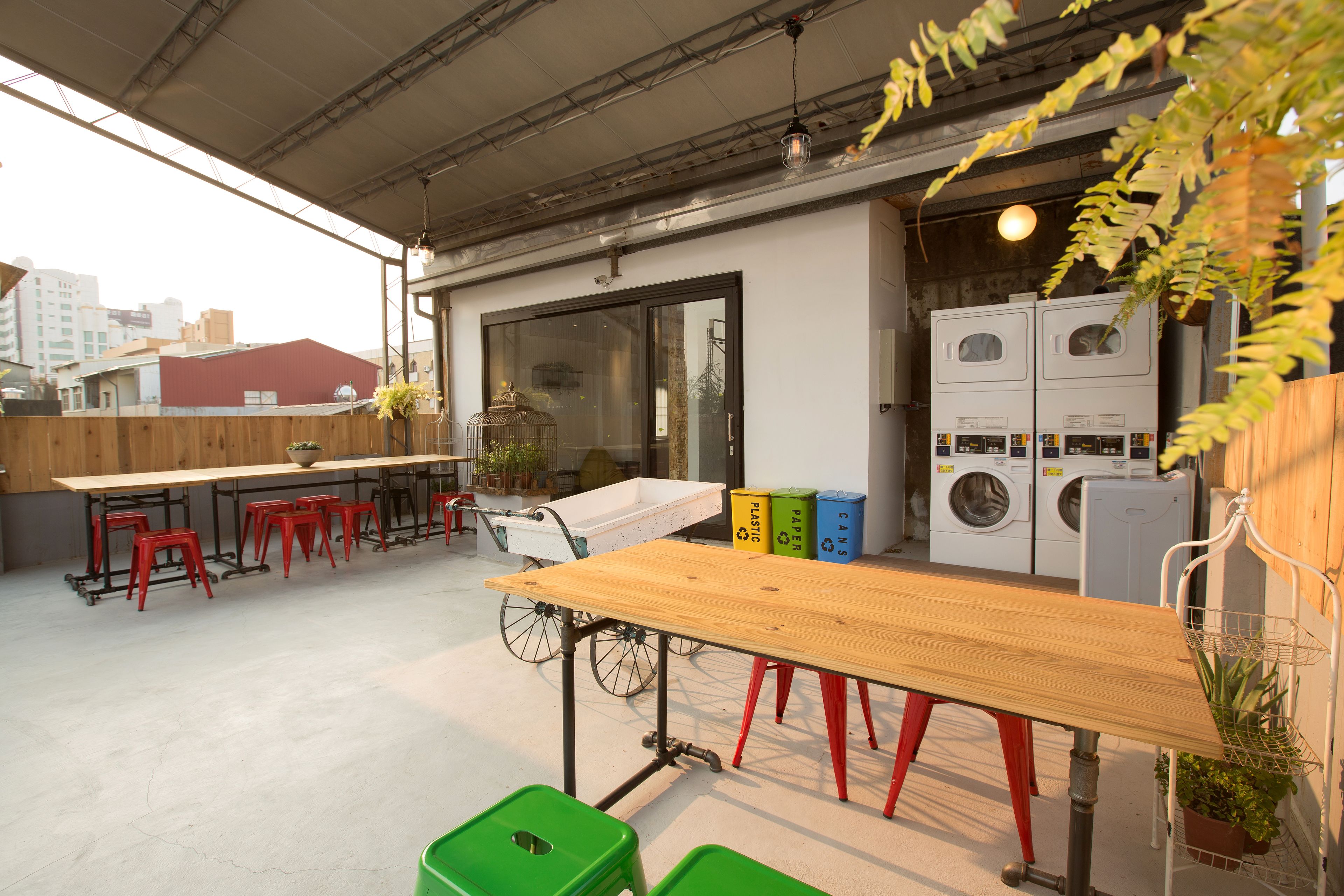A rooftop terrace with a long wooden table, red stools, a bicycle, and a washing machine.