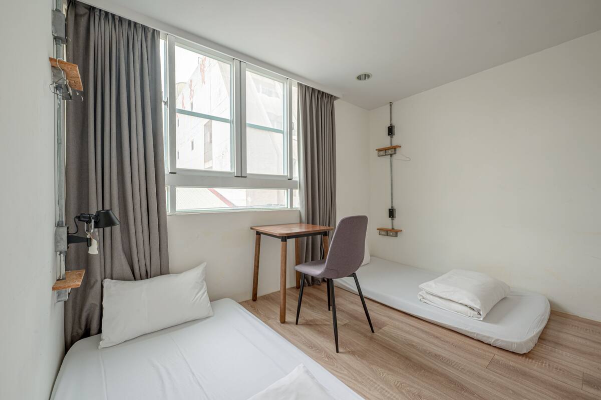 A hotel room with a bed, a desk, a chair, and a window with curtains.