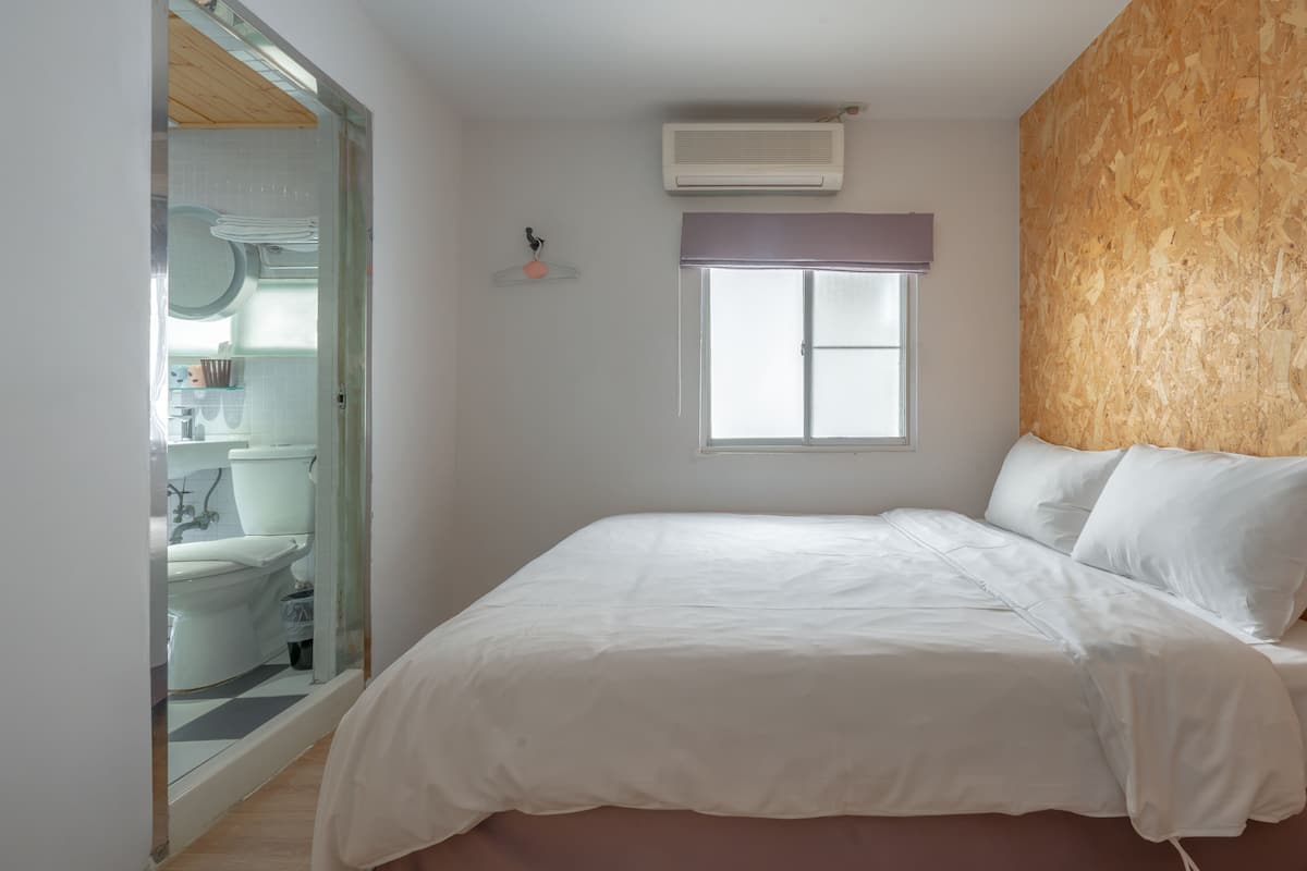 A bedroom with a bed, a window, and a bathroom visible through an open door.