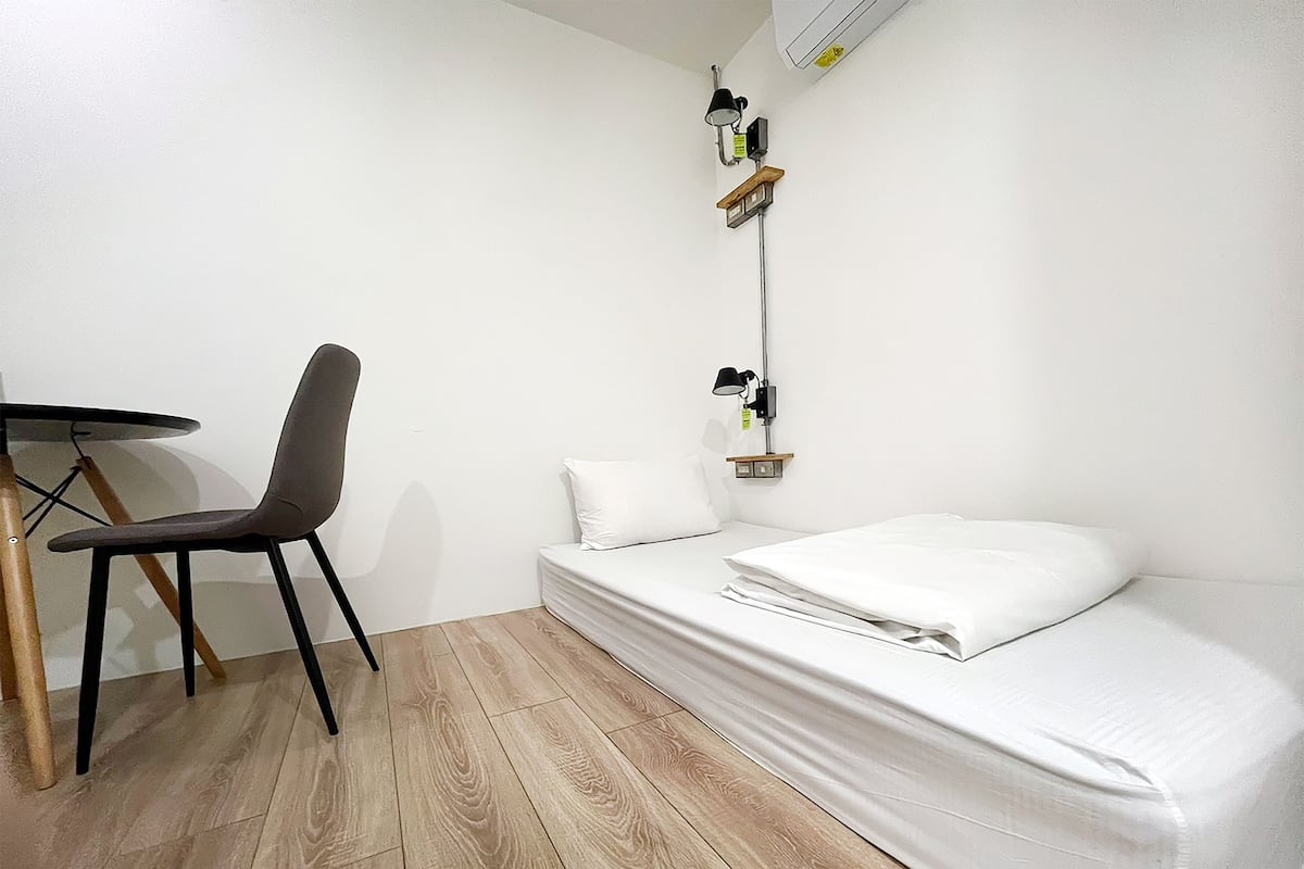 A small, neatly arranged room with a single bed, a chair, and a table.