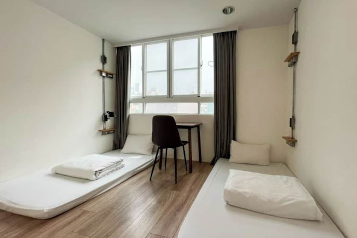 A compact hotel room with a single bed, a small desk, a chair, and a window with curtains.