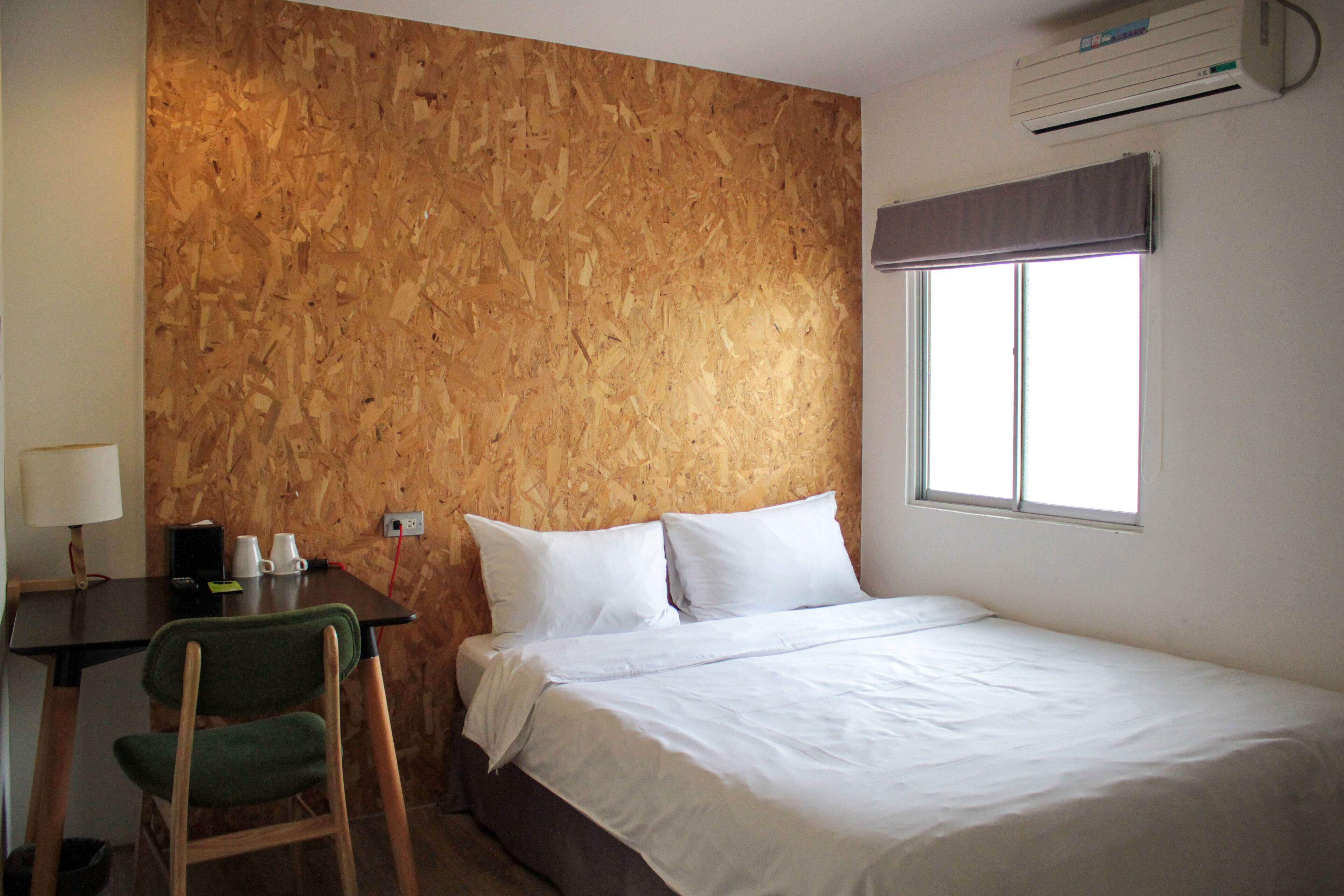 Un dormitorio con pared de madera, una cama, un escritorio con silla y una ventana con persiana.