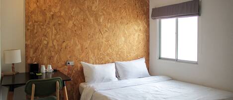 Un dormitorio con pared de madera, una cama, un escritorio con silla y una ventana con persiana.