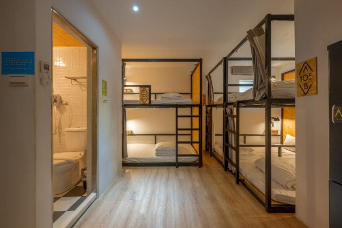 A corridor with bunk beds, a visible bathroom with a toilet, and a door with a sign.