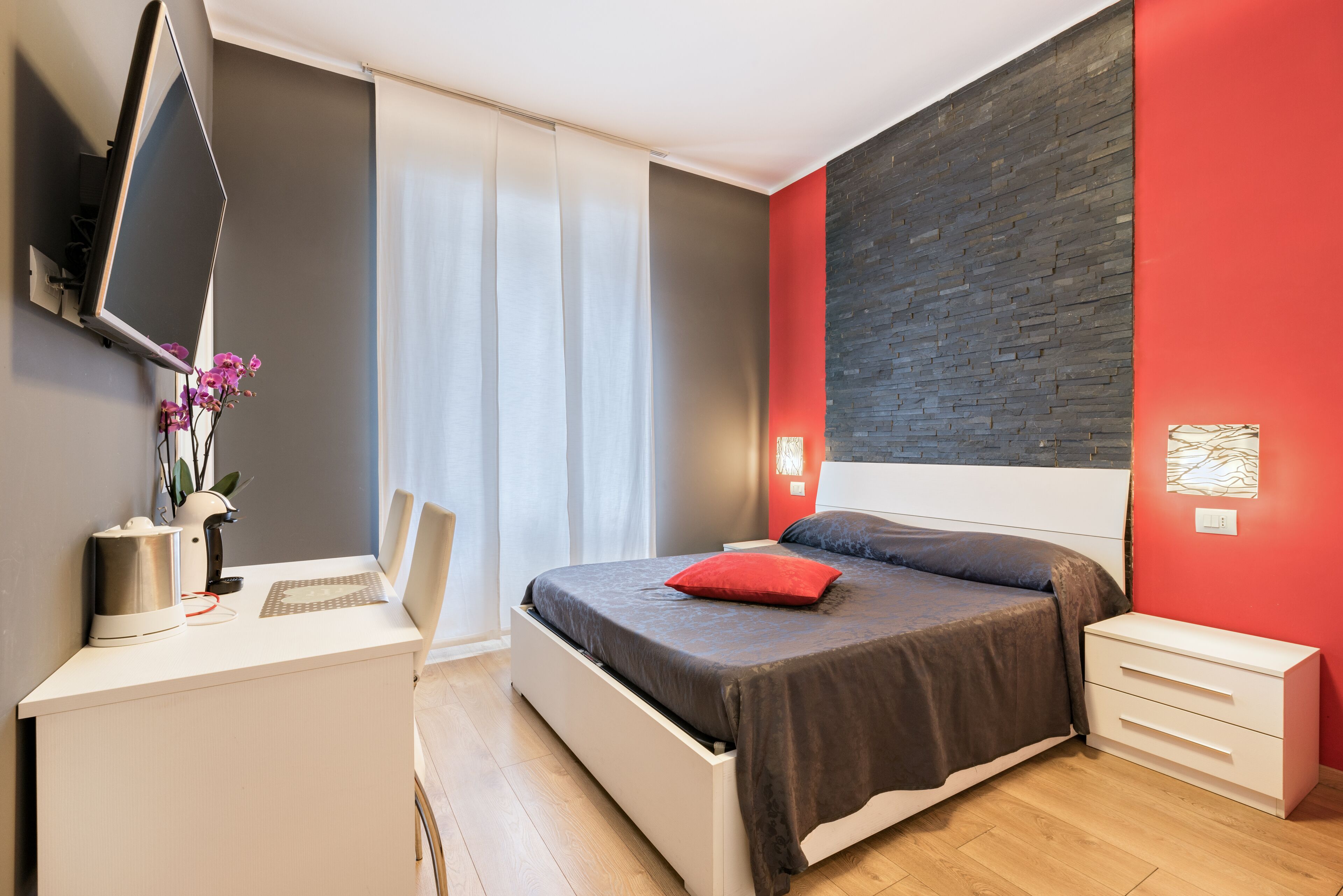 A modern bedroom with a bed, bedside tables, a desk, and a TV.