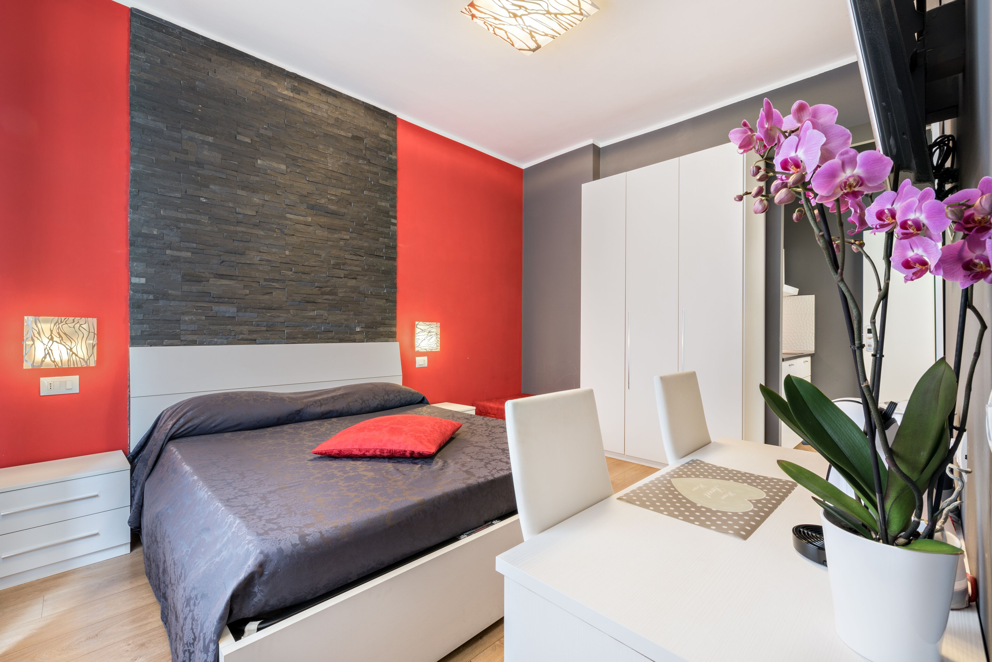 Un dormitorio moderno con cama, escritorio y una orquídea en maceta.