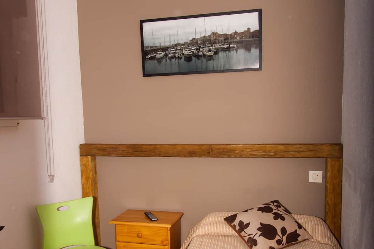 A bedroom with a bed, a wooden nightstand, a green chair, and a framed picture on the wall.