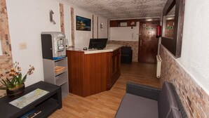 Un área de recepción con una máquina de café, un mostrador, un mapa y una puerta que indica “SALIDA”.