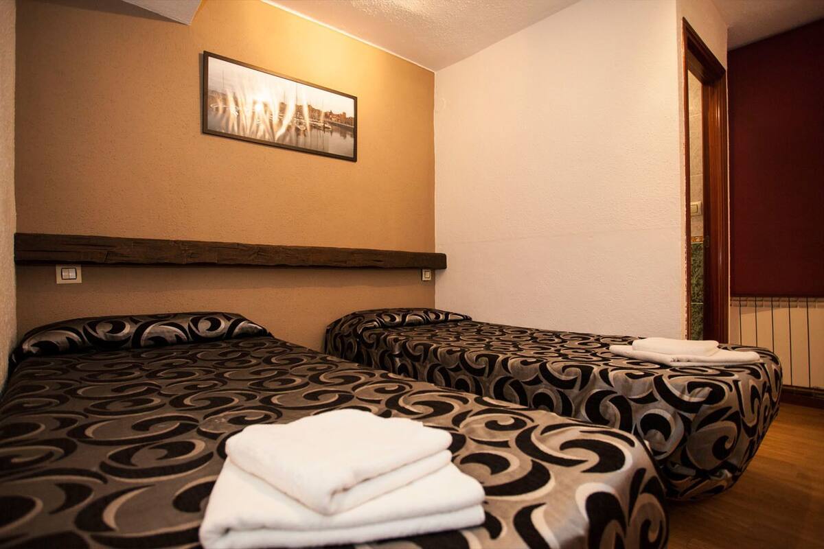 A hotel room with two beds, a wooden headboard, a framed picture on the wall, and a window with a view.