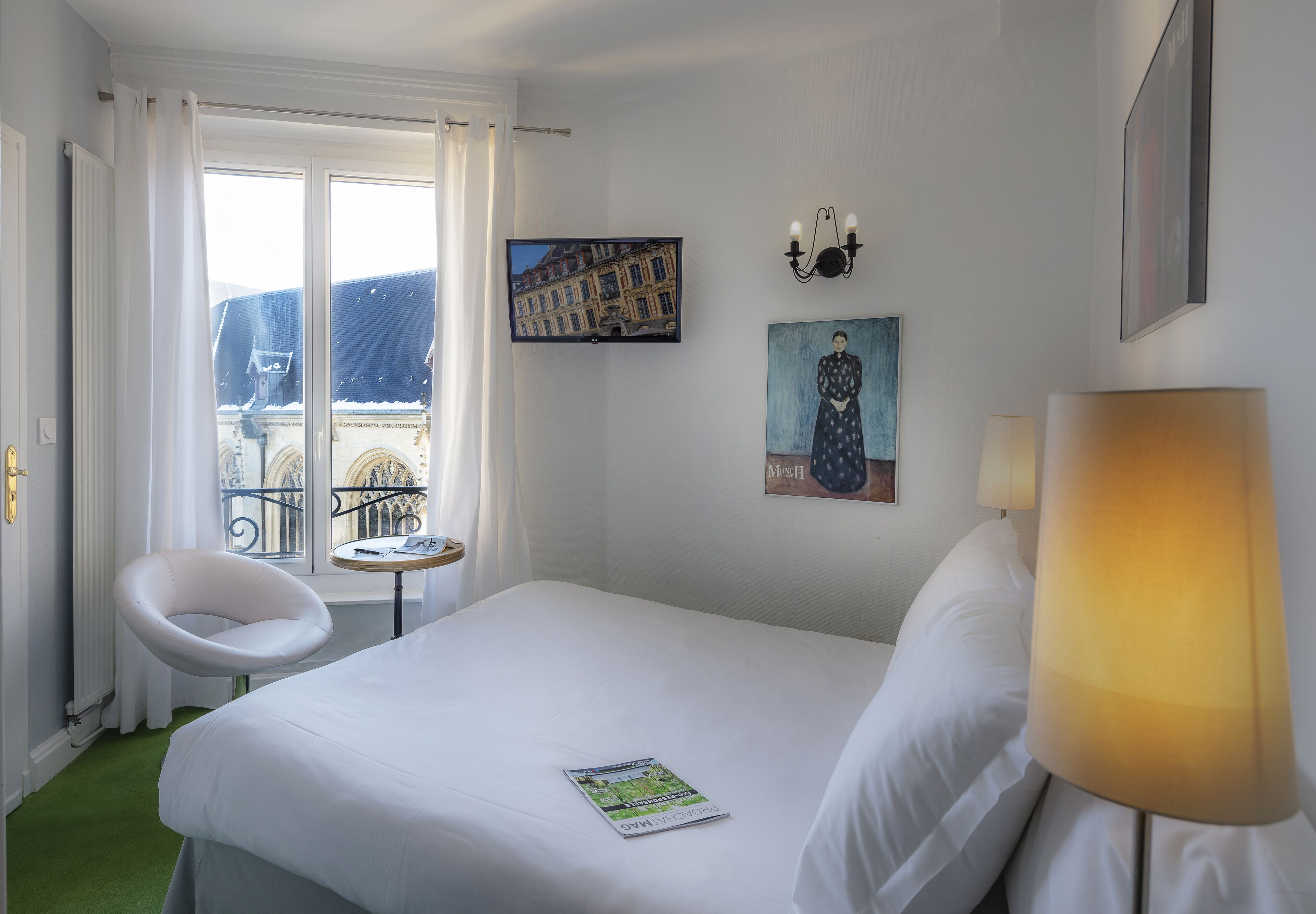 A hotel room with a bed, a chair, a table, and a lamp.