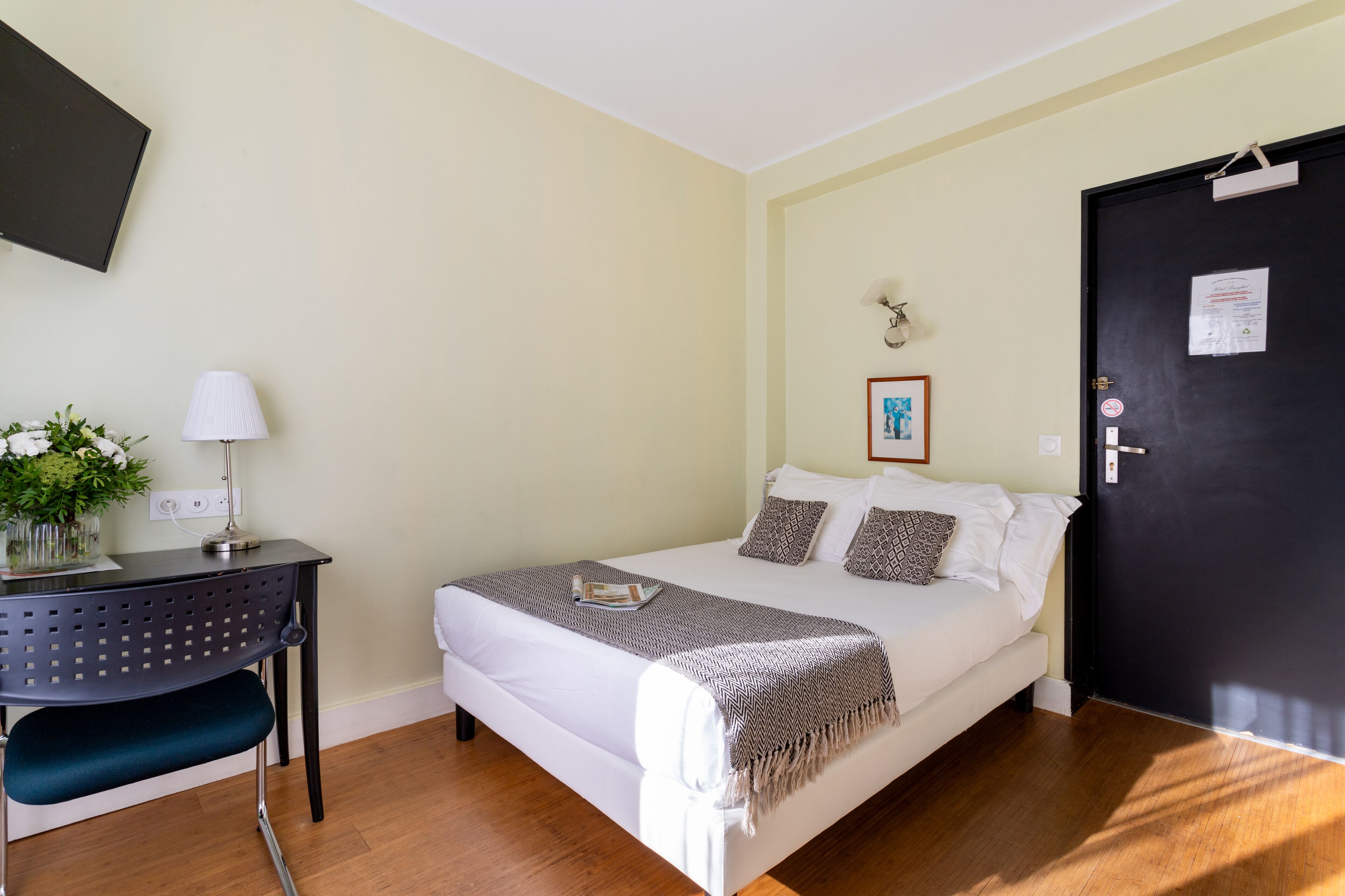 Un dormitorio ordenado con cama, escritorio, silla y puerta.